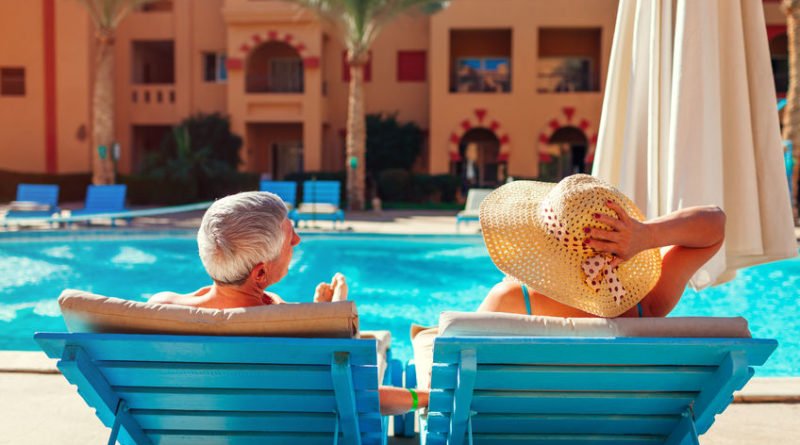 Senior family couple relaxing by swimming pool lying on chaise-longues. People enjoying summer vacation.